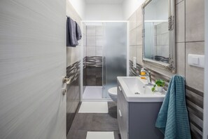 A modern bathroom with a shower, toilet, and sink, featuring a large mirror and a towel rack.