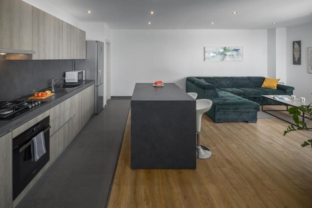 Cocina moderna con encimeras oscuras, una isla central y un comedor con un sofá verde y una mesita.