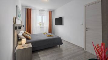 Un dormitorio moderno con cama, mesita de noche, lámpara, cortinas, televisor y puerta.