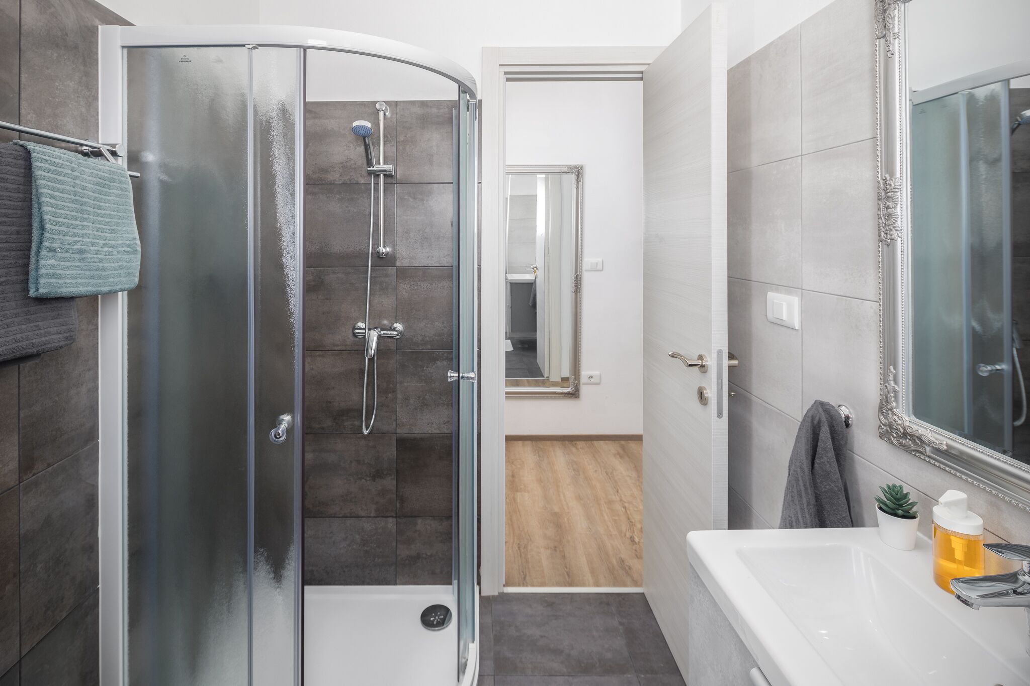 A modern bathroom with a glass-enclosed shower, a white sink with a mirror, and a small potted plant.