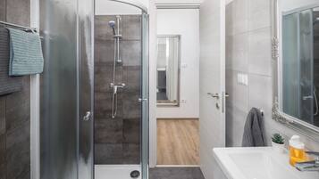 A modern bathroom with a glass-enclosed shower, a white sink with a mirror, and a small potted plant.
