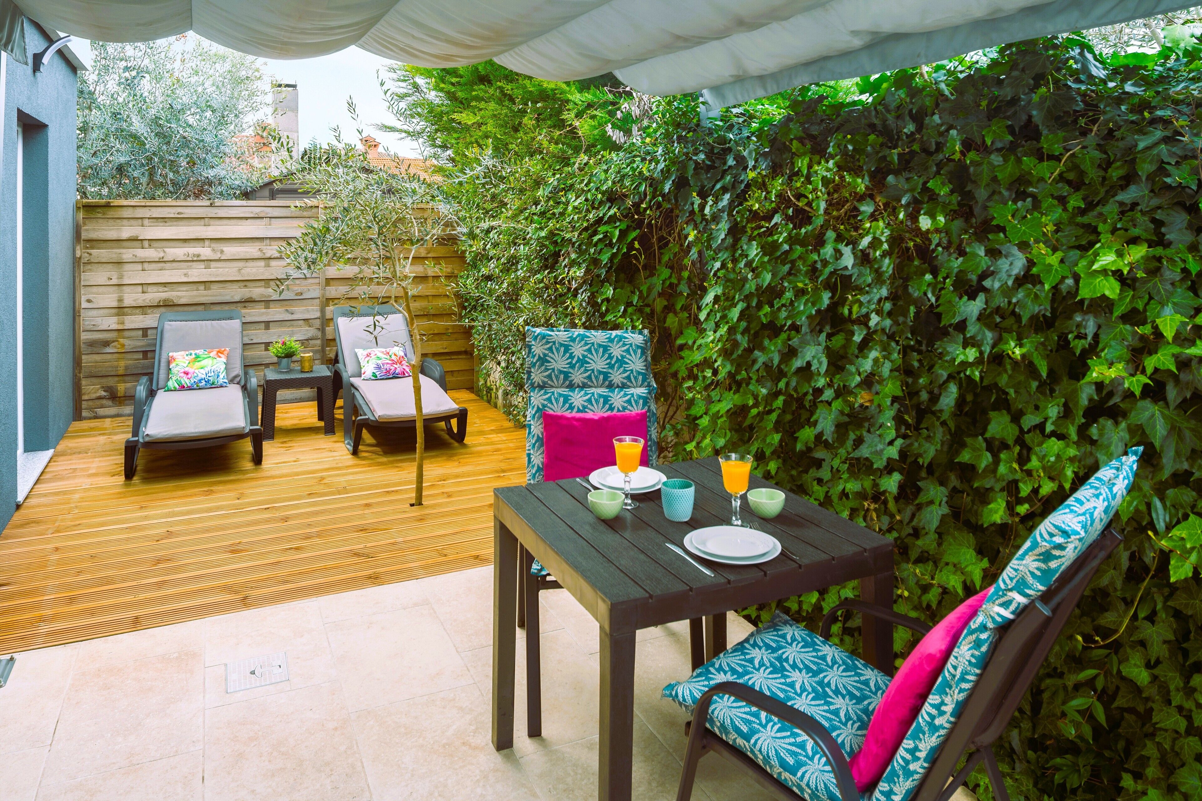 Un patio exterior con una mesa y sillas de madera, suelo de baldosas y una pared cubierta de hiedra.