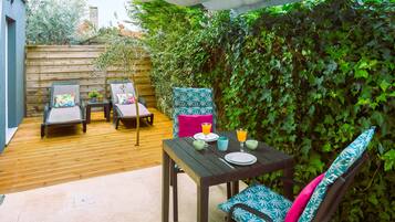 Un patio exterior con una mesa y sillas de madera, suelo de baldosas y una pared cubierta de hiedra.