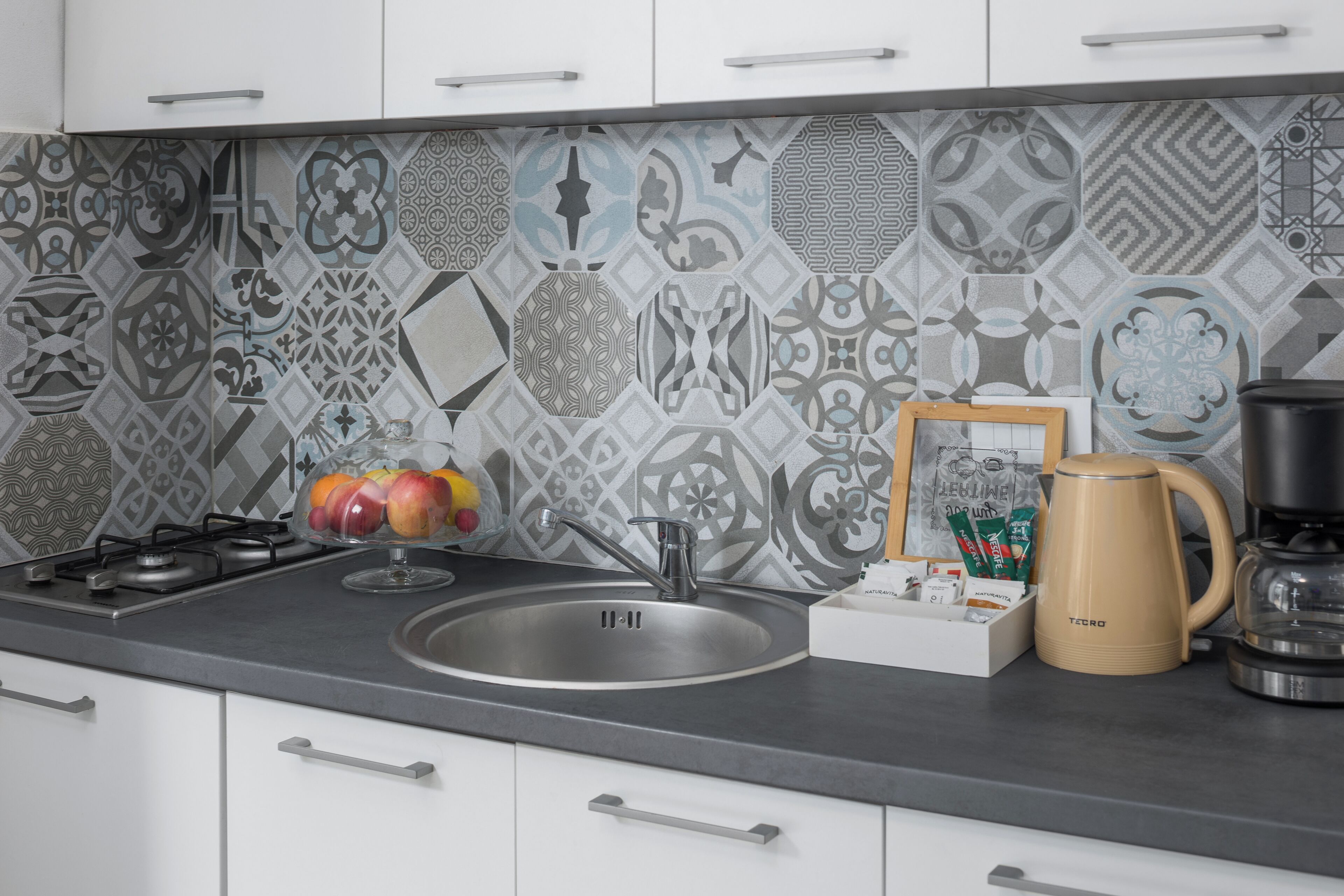 A modern kitchen with a patterned backsplash, stainless steel appliances, and a coffee maker on the counter.