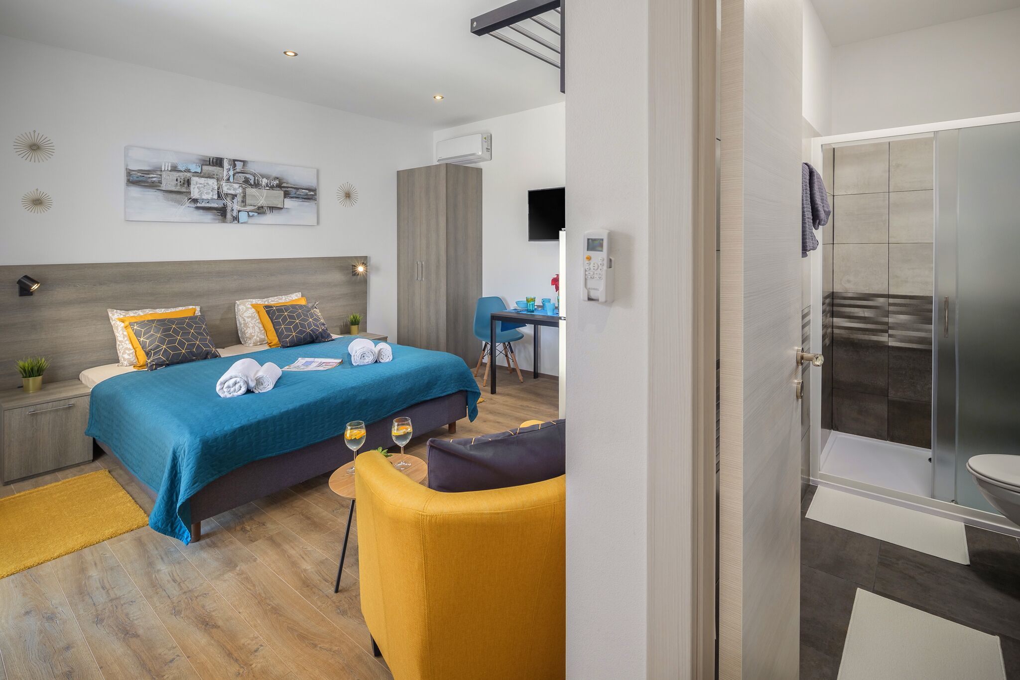 A modern hotel room with a bed, a desk, a chair, and a shower area.