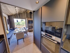 Una cocina moderna con horno Bosch, un comedor con mesa y sillas de vidrio, y vistas al exterior.