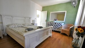 Un dormitorio con una cama grande, un aparador estampado con cebra, una silla de mimbre y un jarrón con flores.