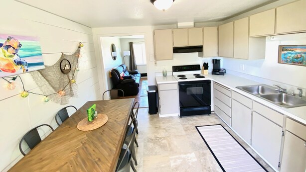 A modern kitchen with white cabinets, a stove, and a sink. There is a dining area with a wooden table and chairs.