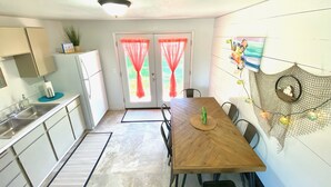 A compact kitchen with a wooden dining table, chairs, a refrigerator, and a sink.