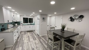A modern kitchen with white cabinets, a granite countertop, and a dining area with a dark wooden table and chairs. - Free 50 Amp EV Charger Modern New, HotTub, A/C, Webber Grill, 2 Decks, FirePit (Fleischmanns)