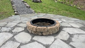 A stone fire pit with a circular design, surrounded by a stone pathway. - Free 50 Amp EV Charger Modern New, HotTub, A/C, Webber Grill, 2 Decks, FirePit (Fleischmanns)