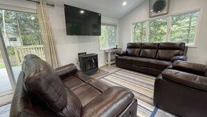 A living room with leather sofas, a flat-screen TV, a fireplace, and large windows. - Free 50 Amp EV Charger Modern New, HotTub, A/C, Webber Grill, 2 Decks, FirePit (Fleischmanns)