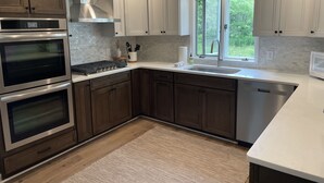A modern kitchen with stainless steel appliances, white cabinetry, and a large window providing a view of greenery outside. - Valley View Lakehouse - Fully updated, dog friendly and beautiful lake view! (Mayville, Chautauqua Lake)