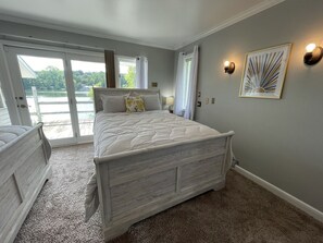 Une chambre à coucher comprenant un lit, une table de chevet, une lampe, une fenêtre avec des rideaux et un luminaire fixé au mur.