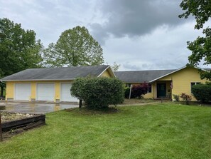 A yellow single-story house with a garage, a front yard, and a small tree.