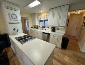A kitchen with white cabinets, a central island with a stove, and a window with curtains. - Pine Lake Retreat on secluded 20 acre nature preserve (Albany)