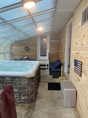 A hot tub area with a stone surround, a wooden wall with a sign, and a bench.