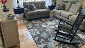 Una sala de estar con dos sofás, una mesita de centro, una alfombra y un sillón mecedora.