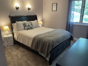 A neatly made bed with a headboard, two bedside lamps, a decorative wall light, and a framed quote on the wall.