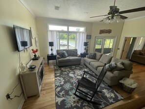 A living room with a sofa, a rocking chair, a television, and a window with a view of a lake.