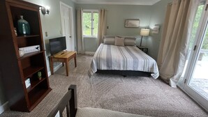 Un dormitorio con una cama, un televisor sobre un soporte de madera, una estantería y una ventana con cortinas.