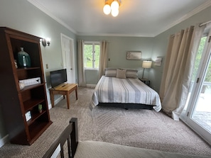 Un dormitorio con una cama, un televisor sobre un soporte de madera, una estantería y una ventana con cortinas.