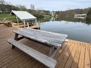 A wooden deck with a picnic table and a covered seating area overlooking a calm lake.