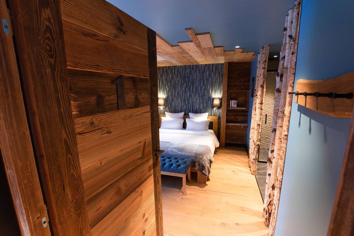 A wooden room with a bed, a bench, and a wall with a textured pattern.