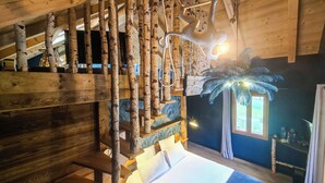 Un interior de madera con una escalera, una cama con ropa blanca y una ventana con cortinas.