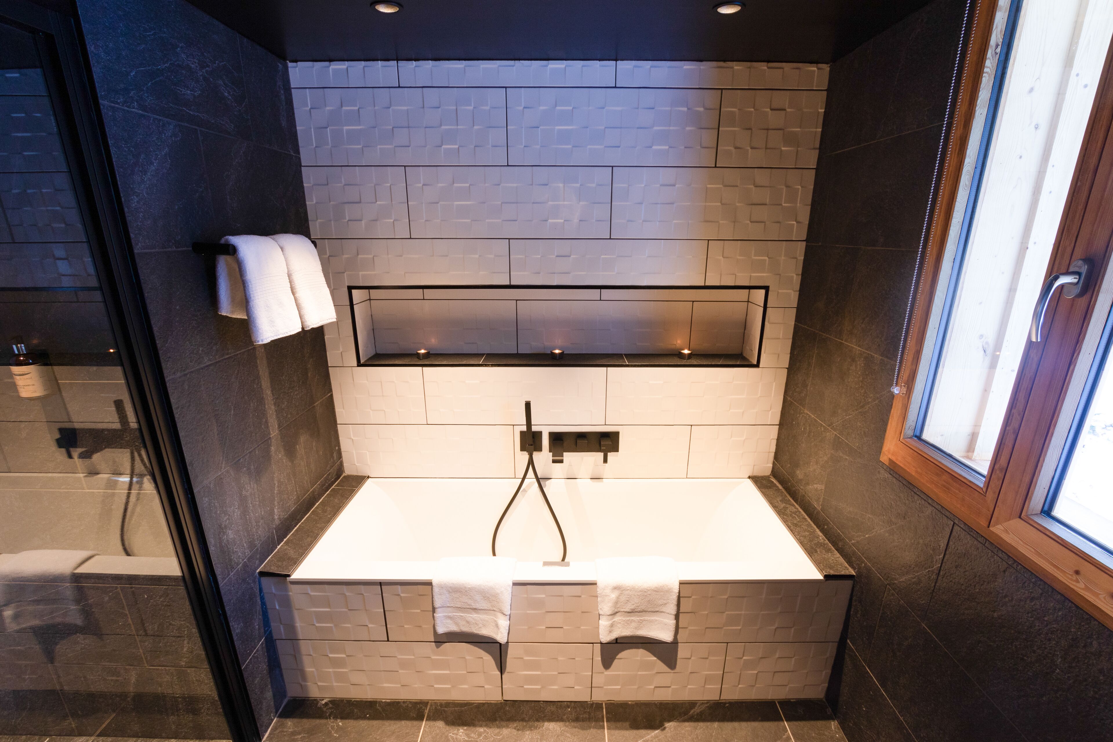 Un baño moderno con una bañera grande, mampara de vidrio y ventana que proporciona luz natural.