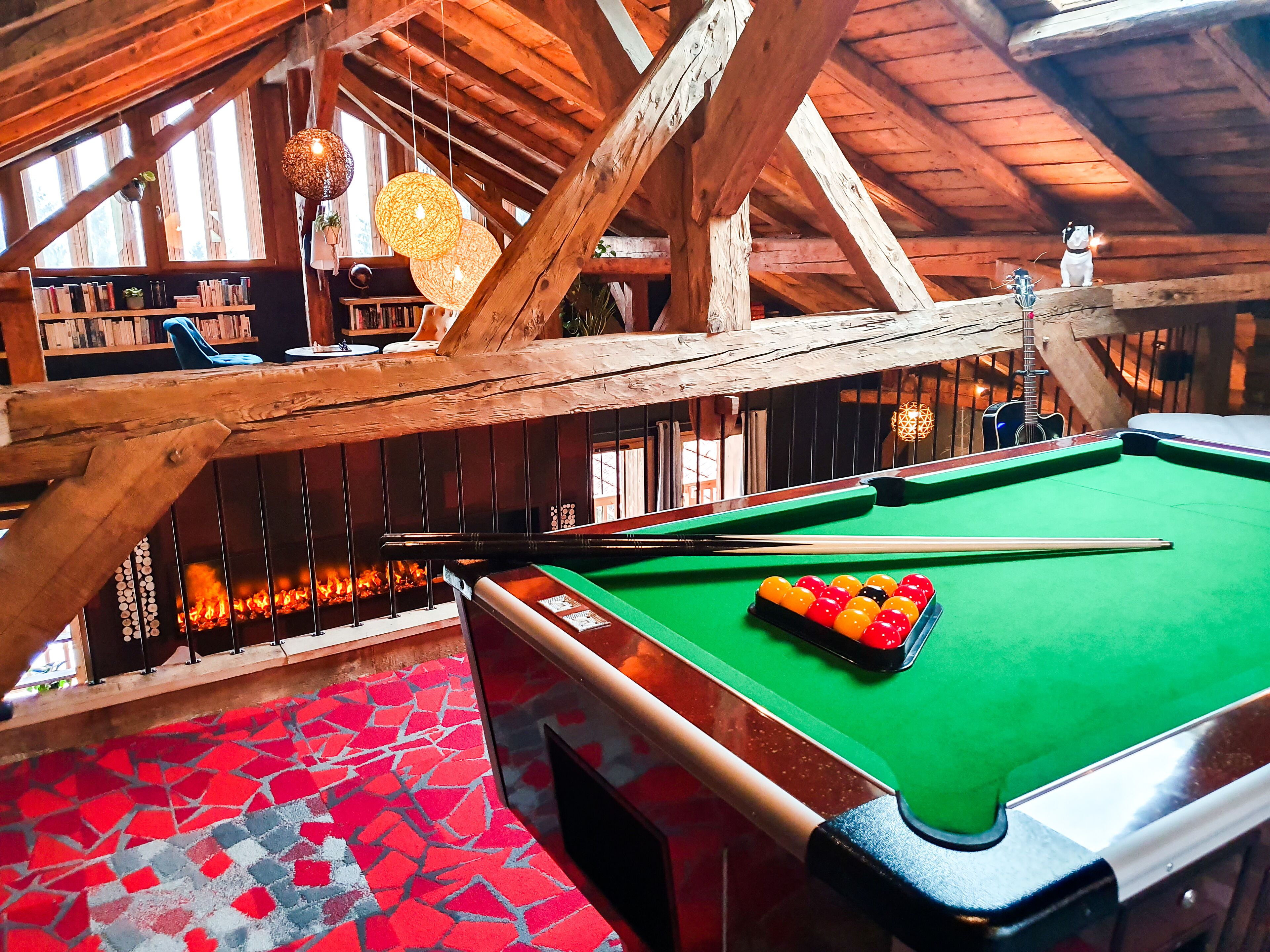 A pool table with a green felt surface, surrounded by wooden beams and a fireplace.