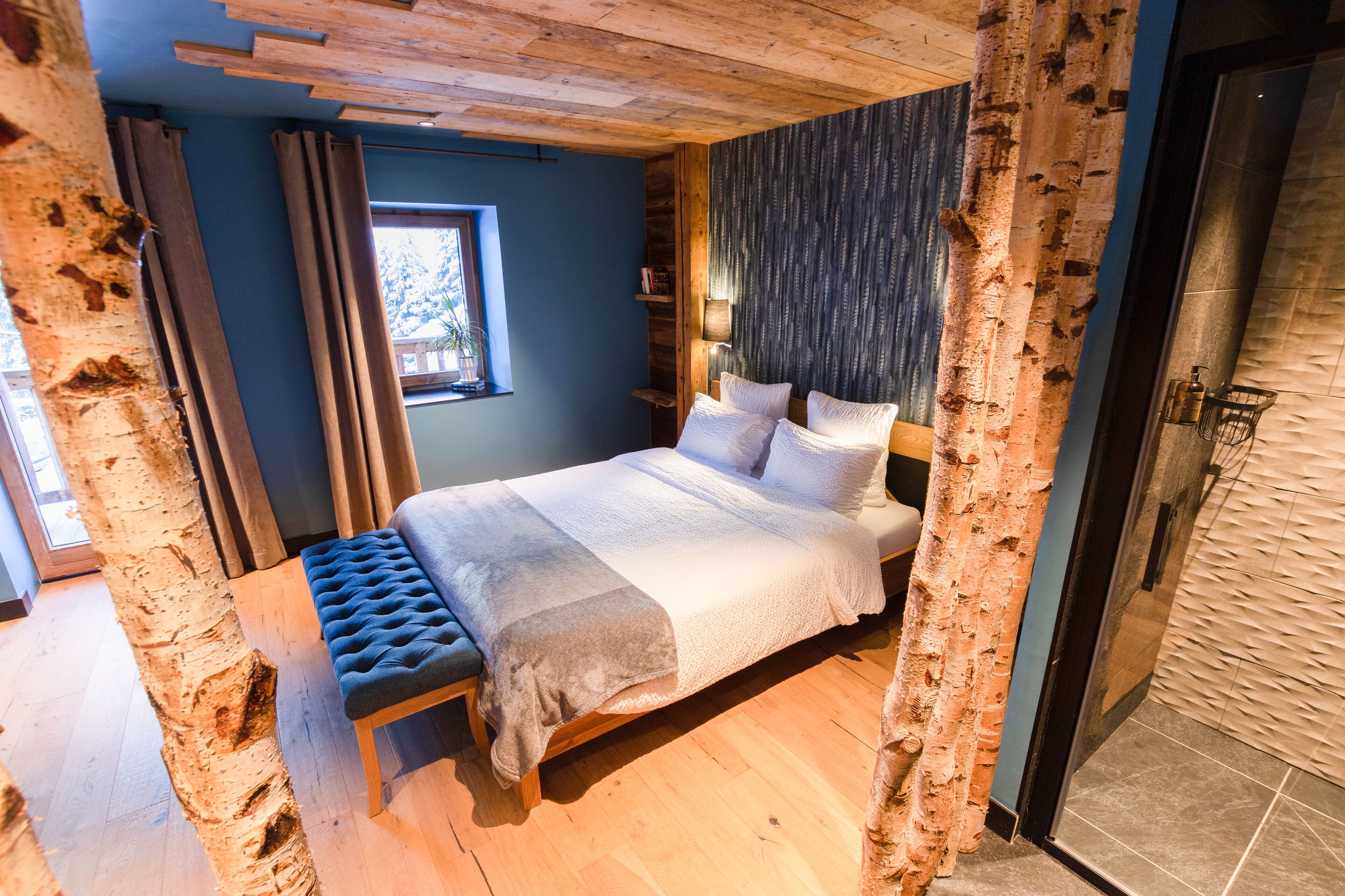 Un dormitorio con cama, banco, ventana y techo de madera.