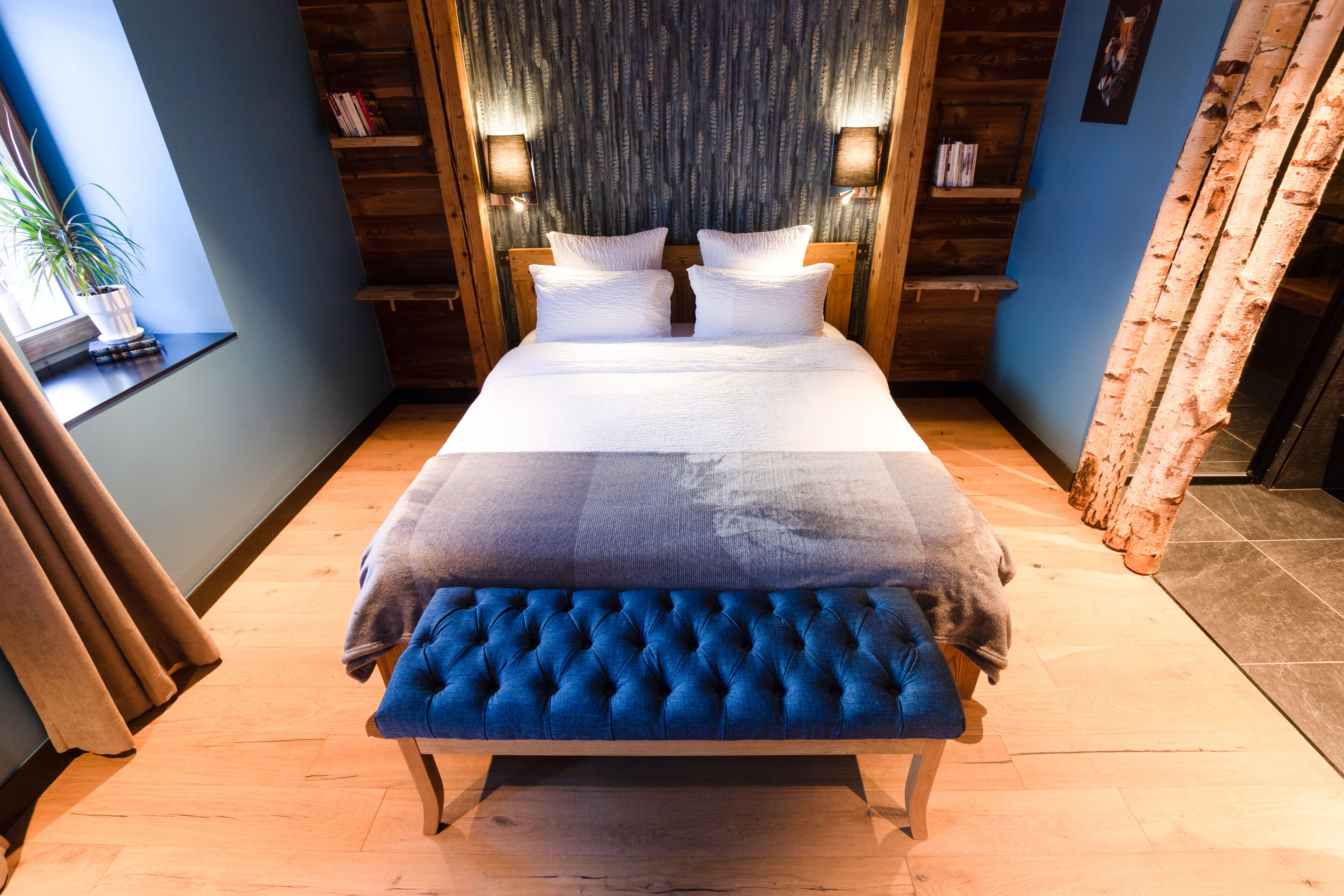 Een slaapkamer met een groot bed, een gestoffeerde bank, een houten hoofdbord en een raam met gordijnen.