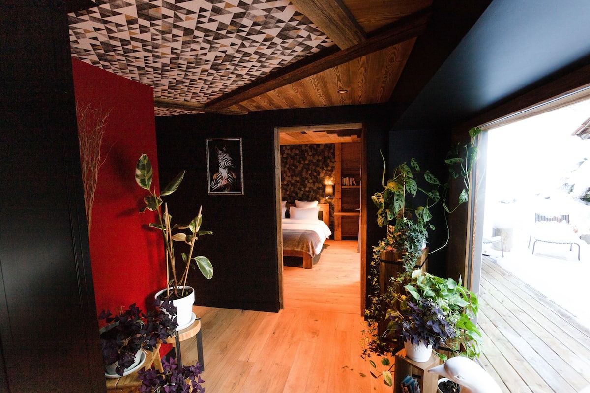A hallway leading to a bedroom with a wooden floor, a red accent wall, and potted plants.