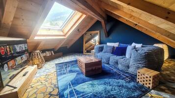 An attic room with a sloped ceiling, a large skylight, a blue sofa, a wooden coffee table, and a patterned rug.