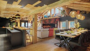 Un interior moderno con cocina, comedor y sala de estar, con vigas de madera, chimenea y un ventanal grande.