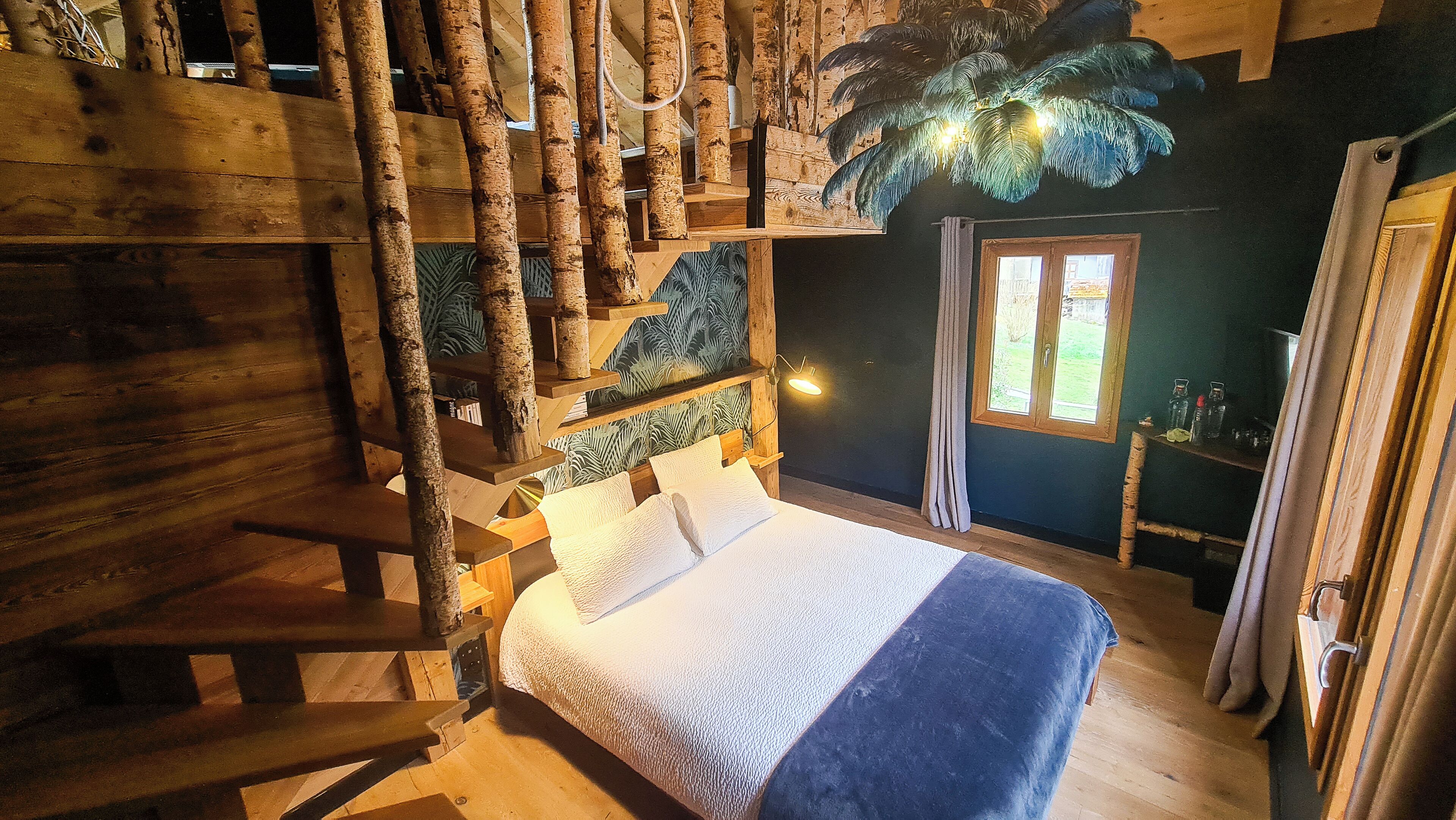 Ein Zimmer aus Holz mit einem Bett, einem Fenster und Blick ins Freie.