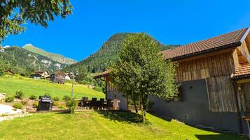 Entorno rural con una casa de madera, mesa de ping pong y montañas al fondo.