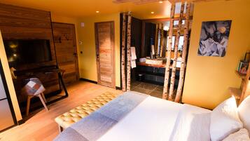 Een slaapkamer met een groot bed, een houten garderobe, een televisie en een badkamer achter een gordijn.