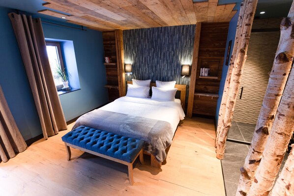 Un dormitorio con una cama grande, un banco, paredes de madera y una ventana con cortinas.