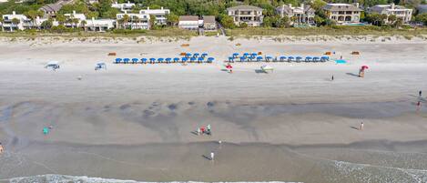 A beach with umbrellas and people, a sandy shore, and houses in the background.