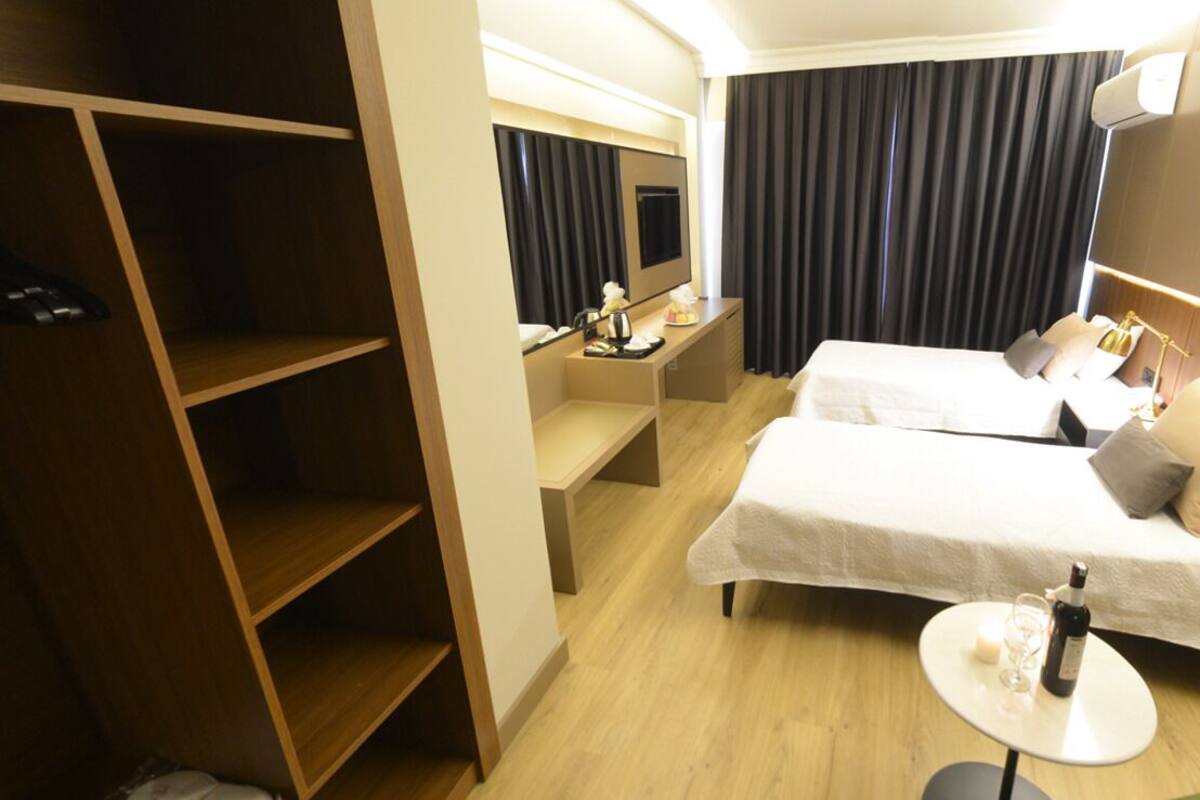 A hotel room with two beds, a small table with a bottle, a TV, and a wardrobe.