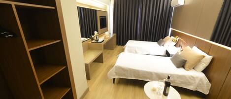 Ein Hotelzimmer mit zwei Betten, einem kleinen Tisch mit einer Flasche, einem Fernseher und einem Kleiderschrank.