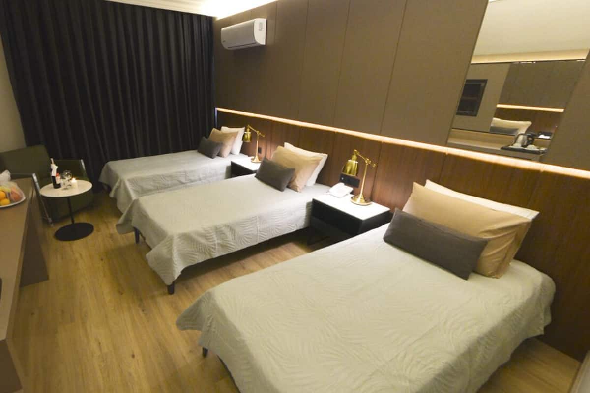 A hotel room with two single beds, a desk with a coffee maker, a small table with a bottle and glasses, and a large mirror on the wall.