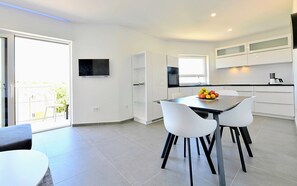 Uma cozinha moderna com armários brancos, uma mesa de jantar com duas cadeiras e uma cesta de frutas sobre a mesa.