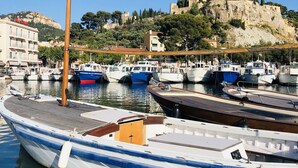 Una marina con barcos amarrados, un muelle de madera y una colina con edificios y árboles al fondo.