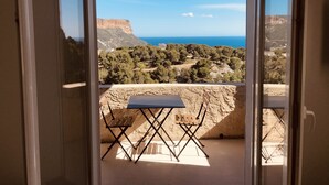 Un balcón con mesa y sillas, con vistas a un paisaje costero con acantilados y el mar.