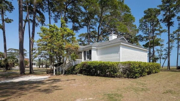 A white single-story house with a covered porch, surrounded by tall trees and a well-maintained lawn.