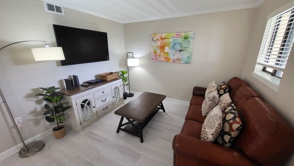 Un salon avec un canapé marron, une table basse, un téléviseur fixé au mur, une lampe sur pied et un tableau.
