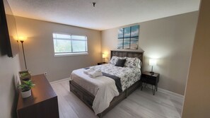 Une chambre à coucher avec un lit, des tables de chevet, une fenêtre, une plante et un tableau au mur.